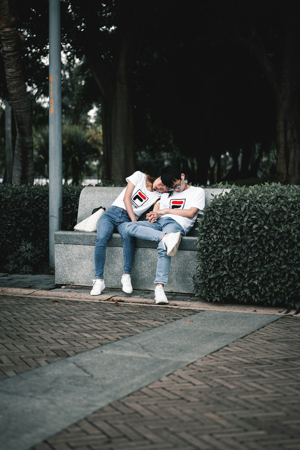 man in white t-shirt and blue denim jeans sitting on gray concrete bench reading book