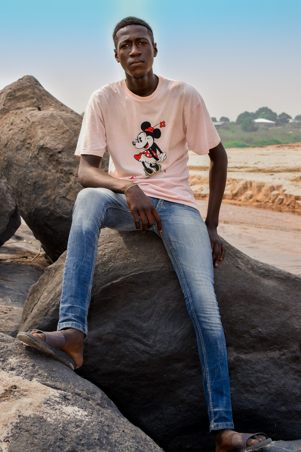 man in white crew neck t-shirt and blue denim jeans sitting on brown rock during