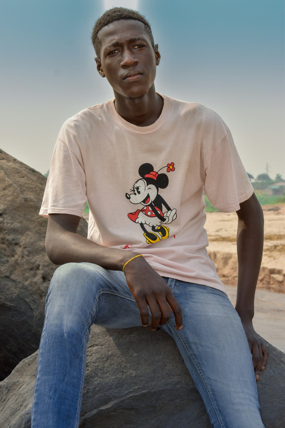 man in white crew neck t-shirt and blue denim jeans sitting on brown rock during