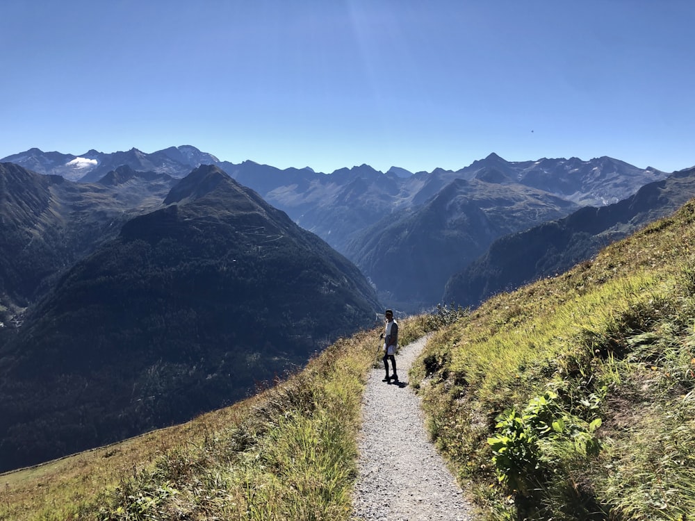 person walking on pathway near green grass field and mountains during daytime