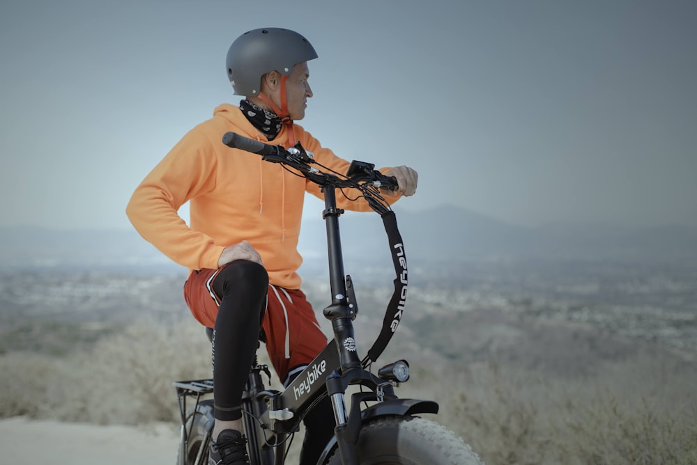 man in orange hoodie and red pants riding black mountain bike