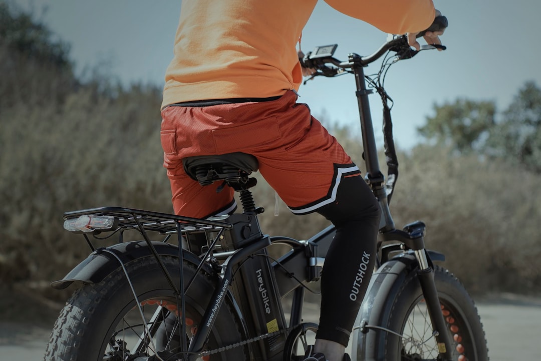 person in orange shirt and black pants riding black bicycle during daytime
