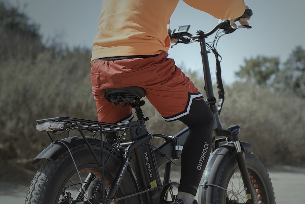 person in orange shirt and black pants riding black bicycle during daytime