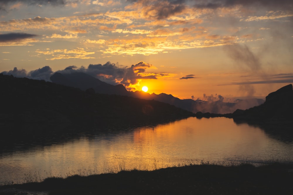 silhouette of mountains near body of water during sunset