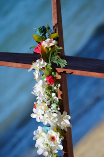 Close-up of a beautifully crafted wooden cross beside a roadside shrine adorned with flowers.