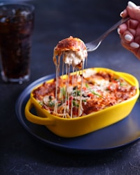 person holding stainless steel fork and yellow bowl with food