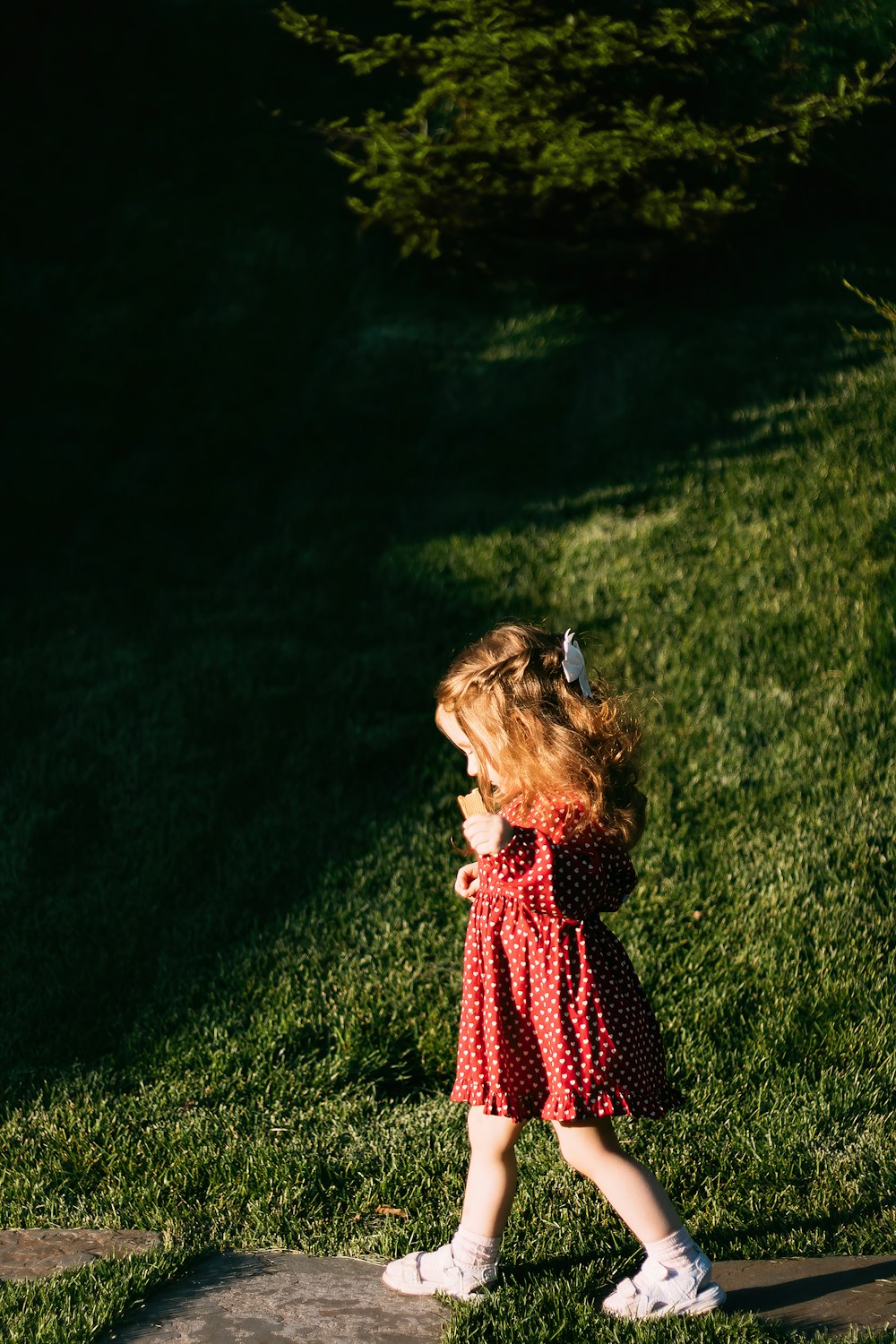 menina no vestido vermelho e preto que está em pé no campo verde da grama durante o dia