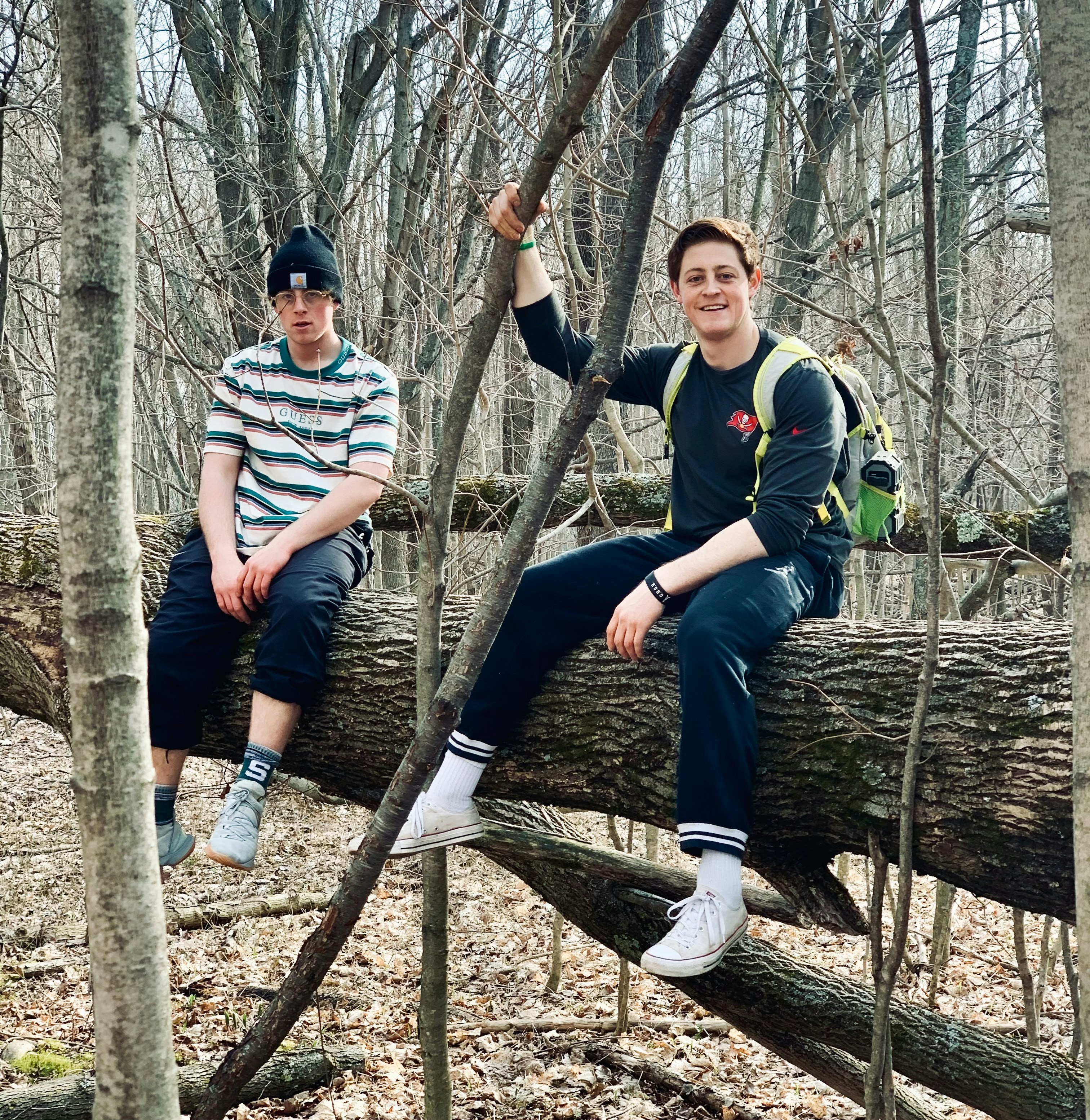 two young men sitting on a fallen tree in the woods