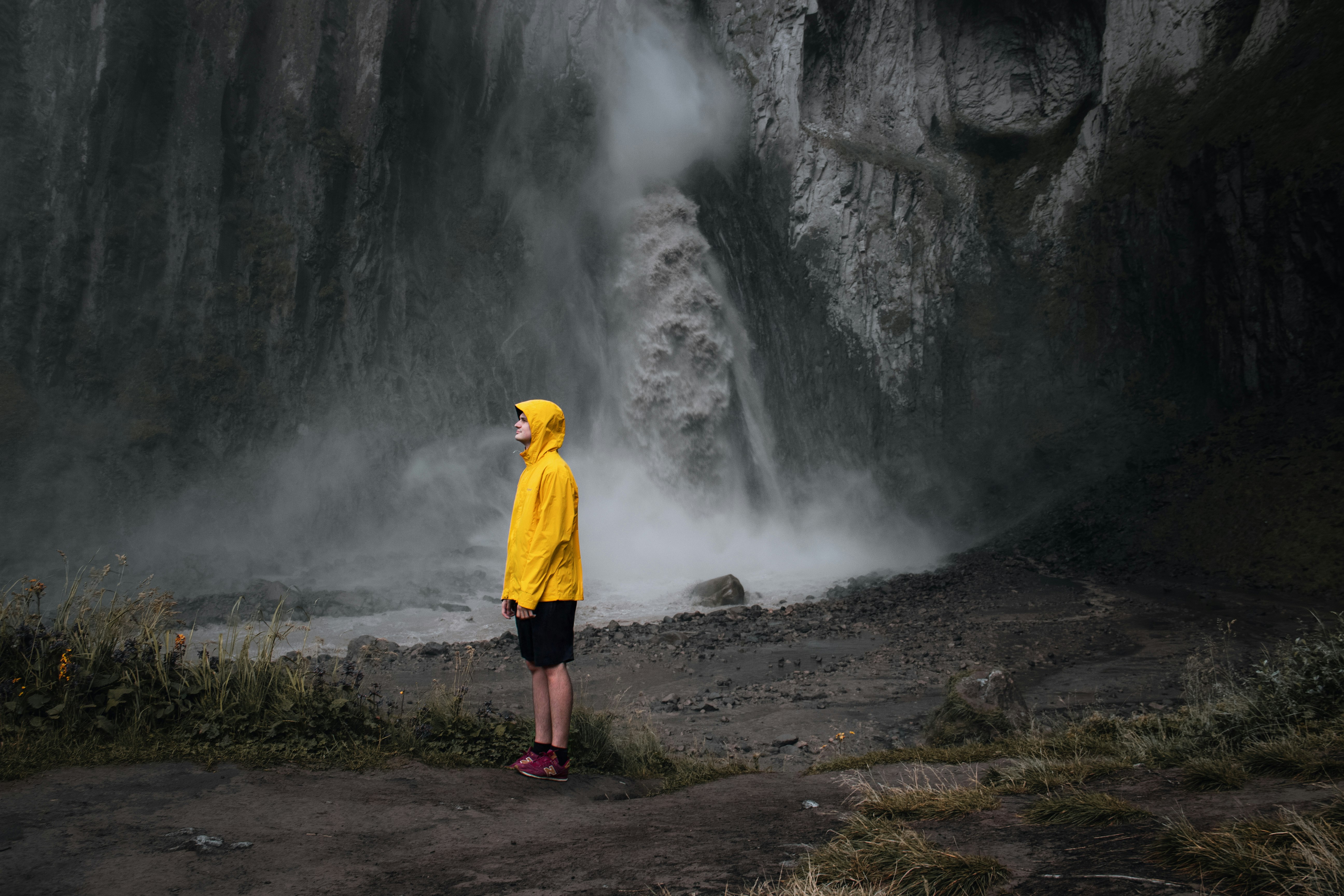 man in yellow hoodie standing near waterfalls during daytime