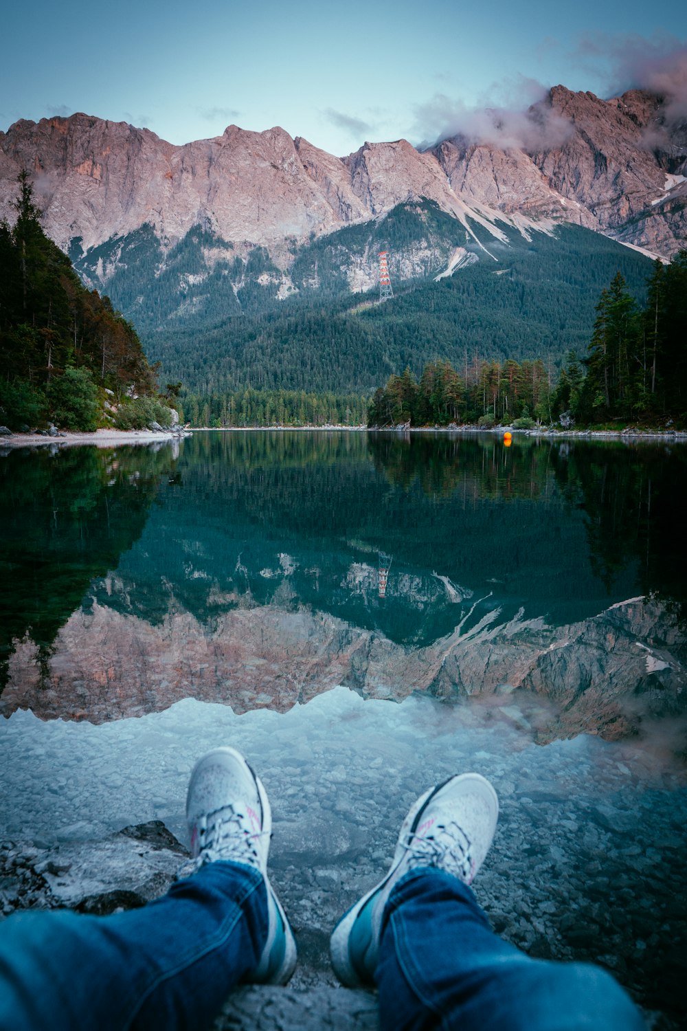 person in white sneakers sitting on rock near lake during daytime