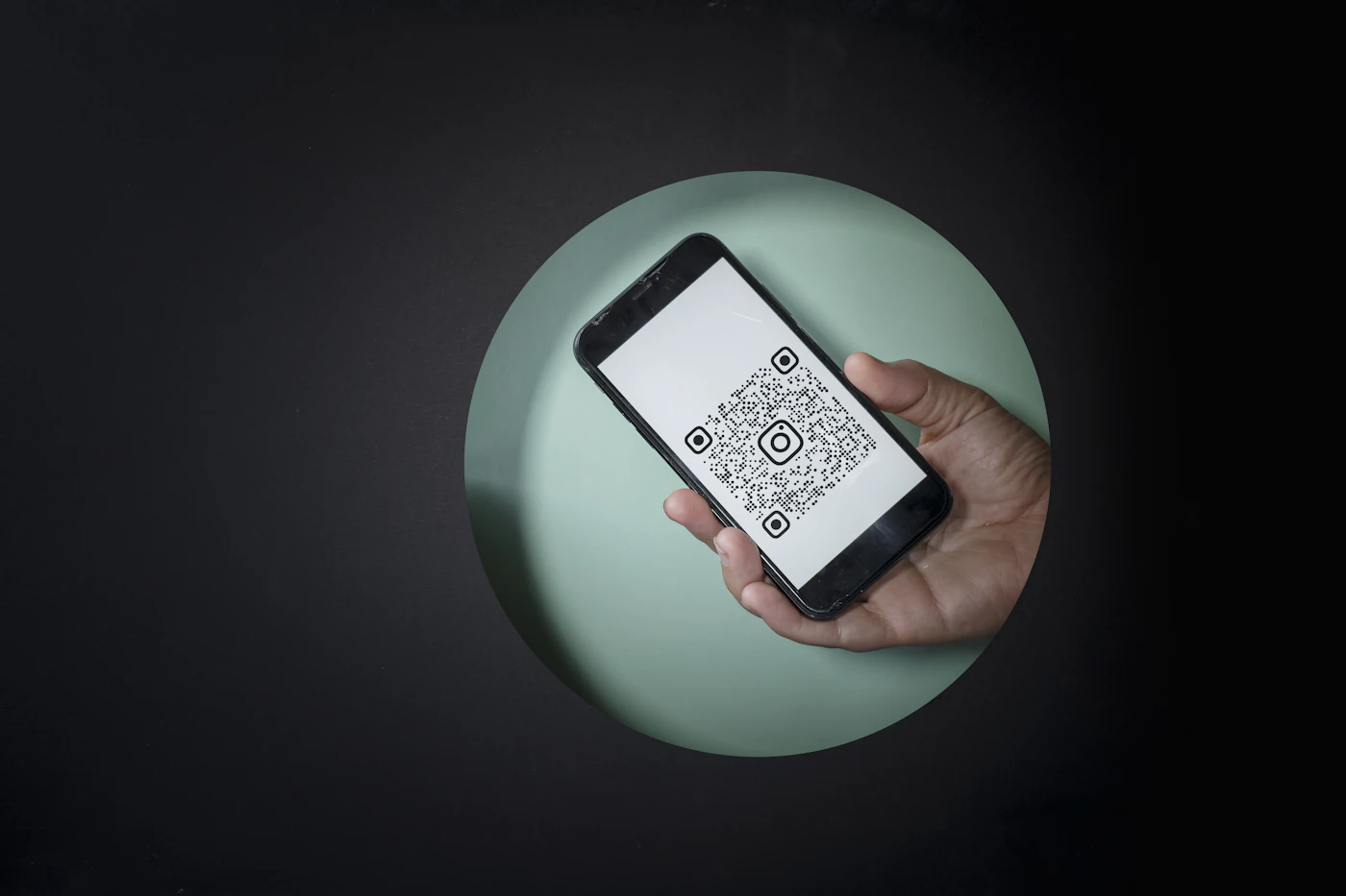 A hand holds a smartphone showing a QR code against a dark background