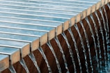 Water flows uniformly over the edge of a structure composed of evenly spaced, parallel metal bars into a basin below.
