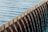 Water flows uniformly over the edge of a structure composed of evenly spaced, parallel metal bars into a basin below.