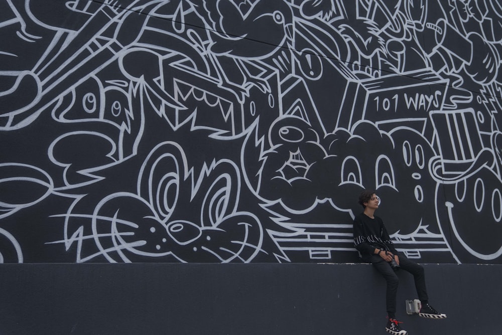 man in black jacket standing beside wall with graffiti