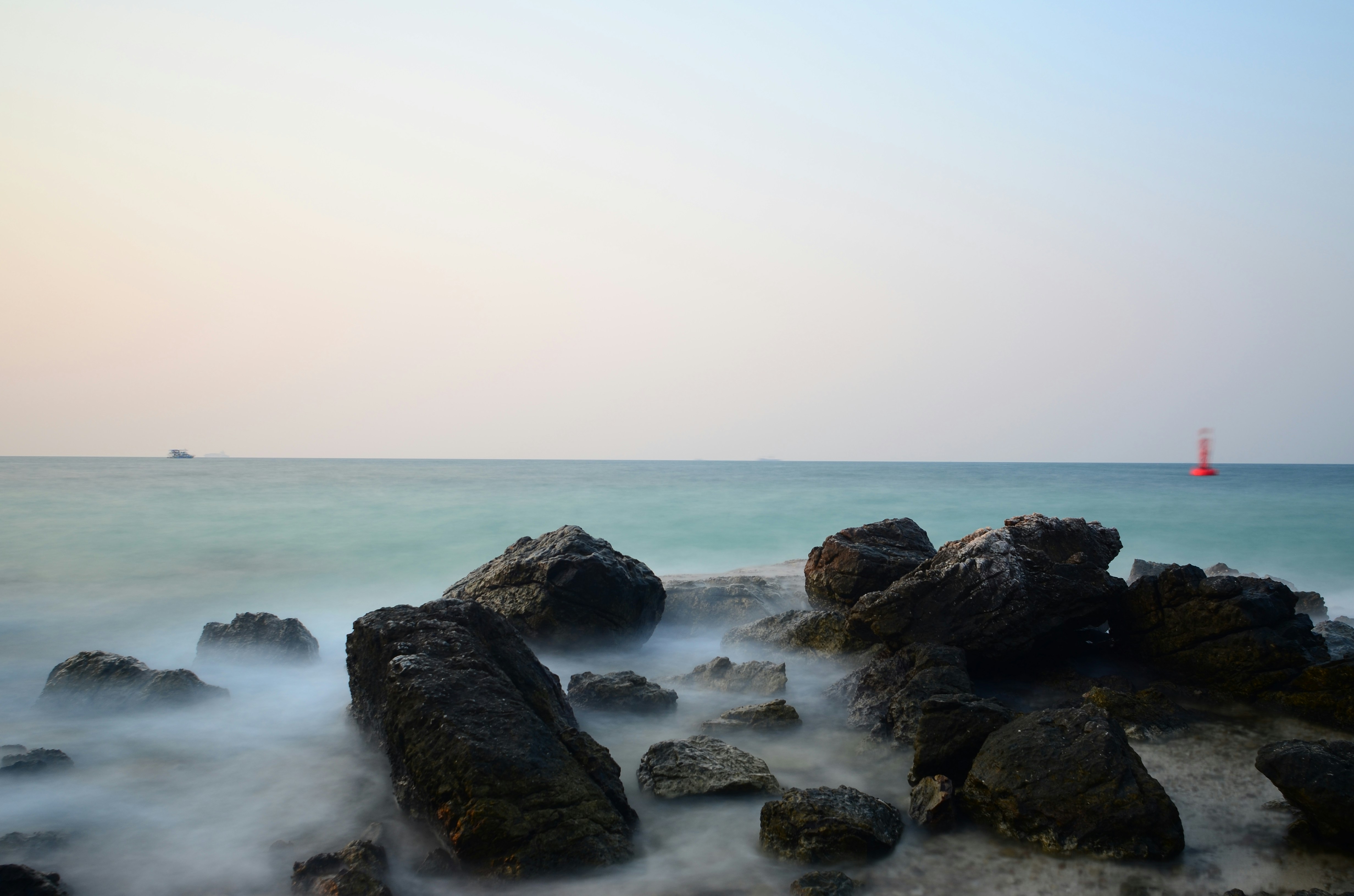 Rocky shoreline with gentle waves and distant sailboat