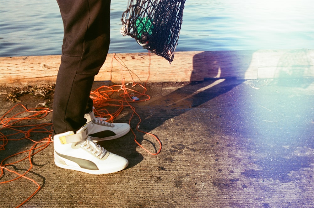 person in black pants and white sneakers standing on brown wooden dock during daytime