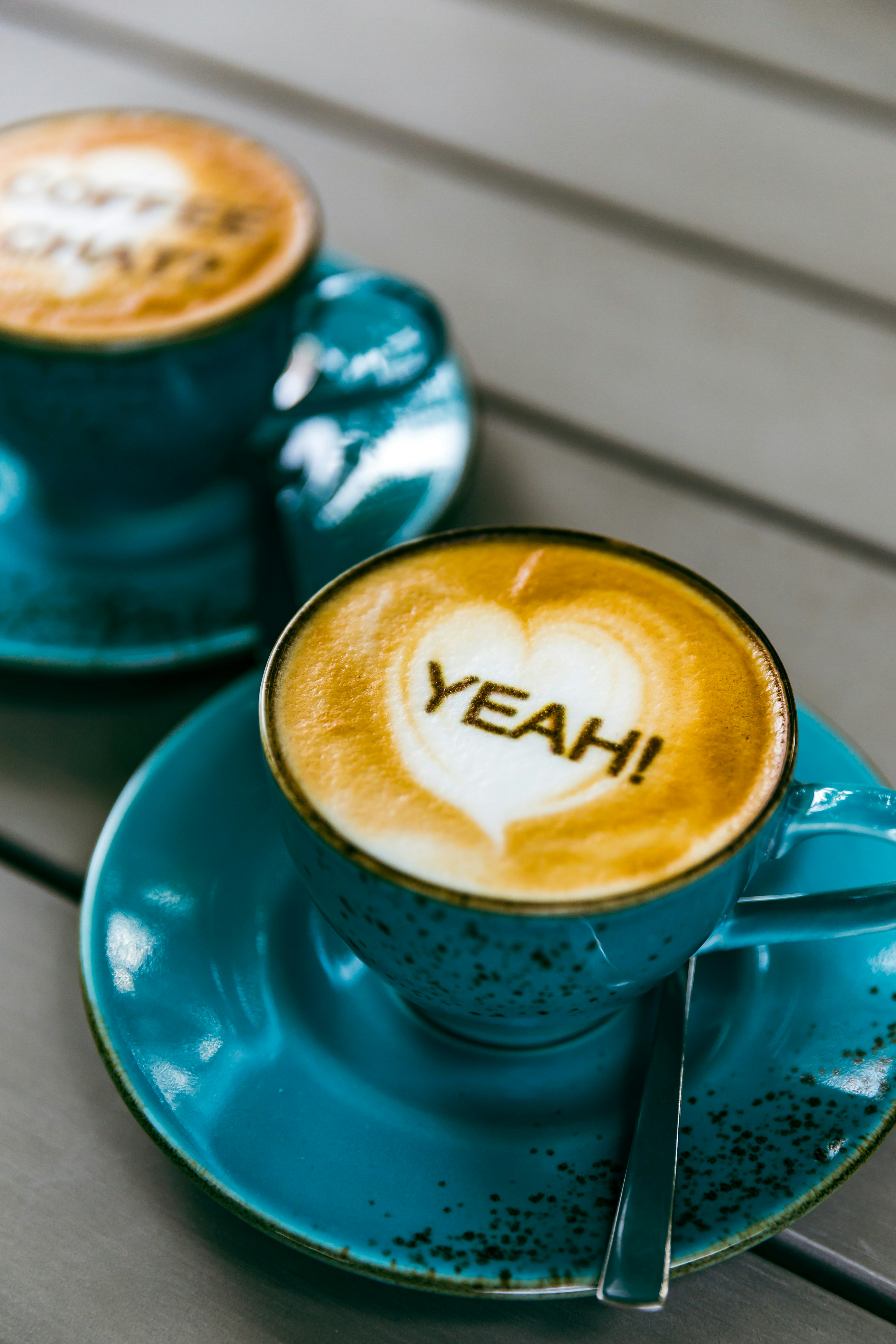 Communication by coffee. Two cups of freshly brewed coffee (cappuccino) on a table, with the following text on the coffee foam: \