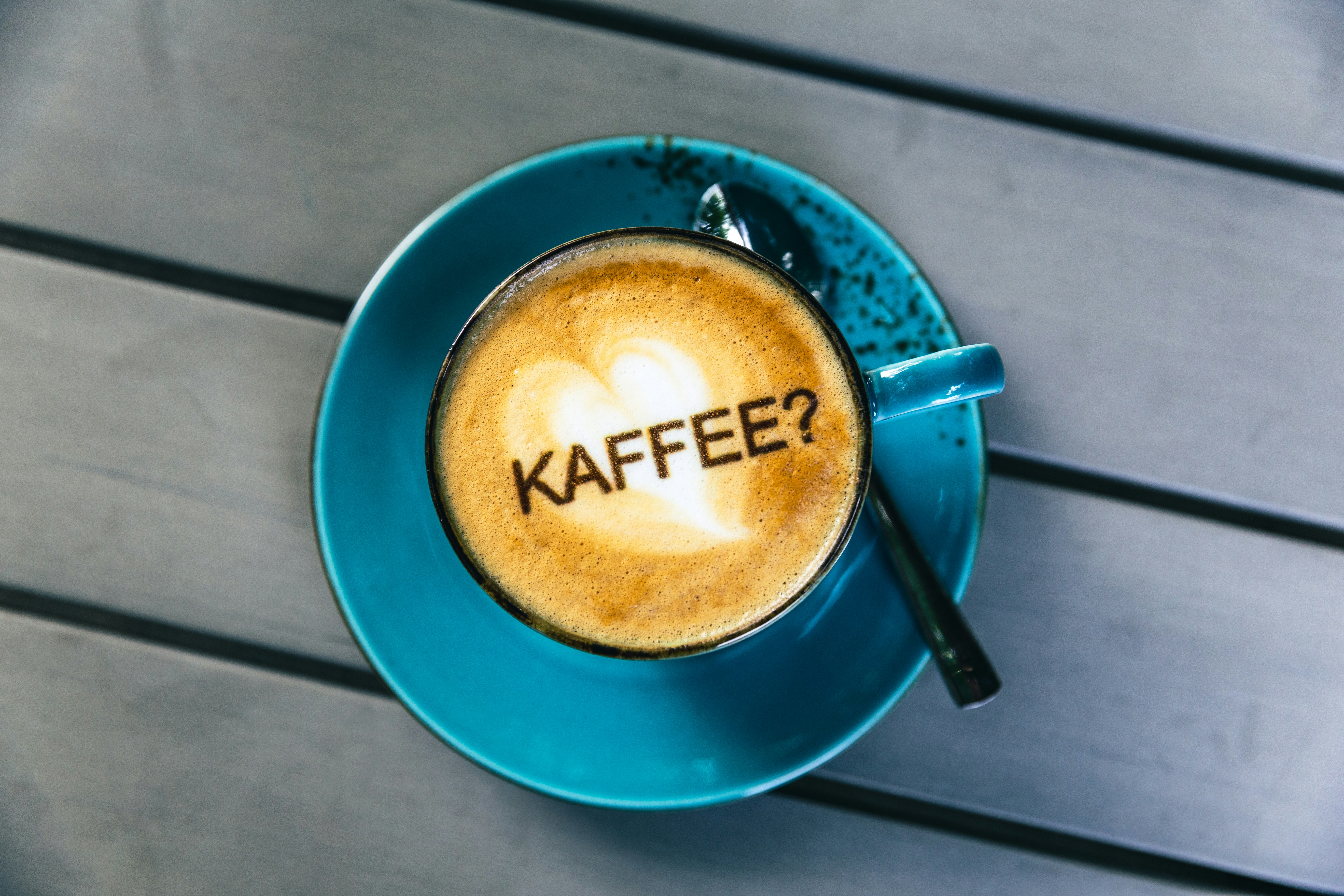 Communication by coffee.

One cup of freshly brewed coffee (cappuccino) on a table, with the following text in GERMAN language on the coffee foam: "KAFFEE?" (English: "Coffee?"). The food coloring was applied to the milk foam by a professional barista coffee printer.