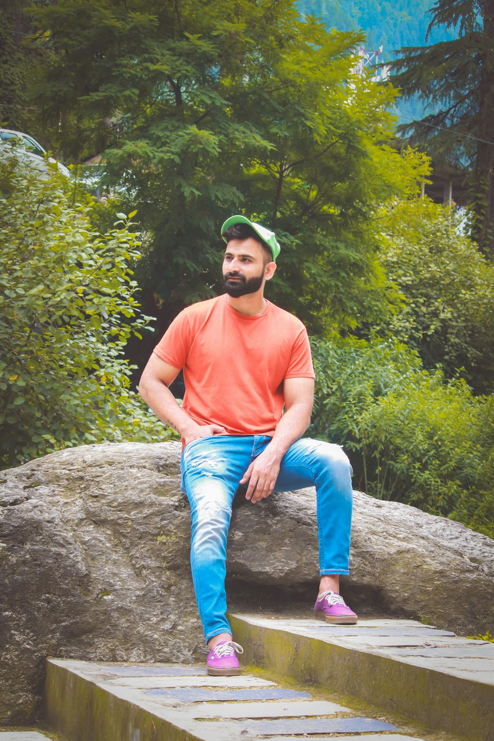man in red crew neck t-shirt and blue denim jeans sitting on gray rock during