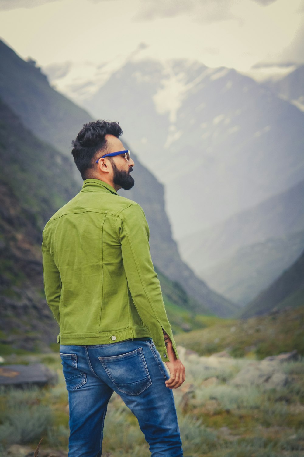 man in green long sleeve shirt and blue denim jeans standing on mountain during daytime