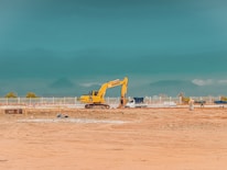 yellow excavator on brown sand under blue sky during daytime