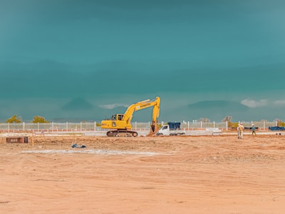 yellow excavator on brown sand under blue sky during daytime