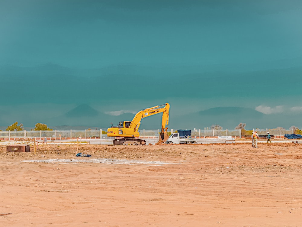 excavadora amarilla en arena marrón bajo cielo azul durante el día