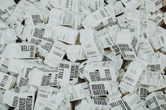 A large number of white cartons with black text saying 'Boxed Water is Better' are piled together. The cartons have graphics and text promoting sustainability.