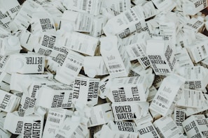 A large number of white cartons with black text saying 'Boxed Water is Better' are piled together. The cartons have graphics and text promoting sustainability.