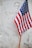 A small American flag is planted in front of a white marble gravestone with the word 'UNKNOWN' and 'U.S.' inscribed on it, along with a cross engraved near the top.