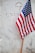 A small American flag is planted in front of a white marble gravestone with the word 'UNKNOWN' and 'U.S.' inscribed on it, along with a cross engraved near the top.
