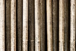Vertical metal rods with a textured and weathered appearance, aligned in parallel and closely packed together.