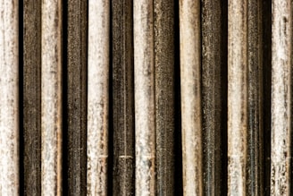 Vertical metal rods with a textured and weathered appearance, aligned in parallel and closely packed together.