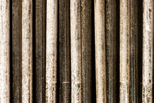 Vertical metal rods with a textured and weathered appearance, aligned in parallel and closely packed together.