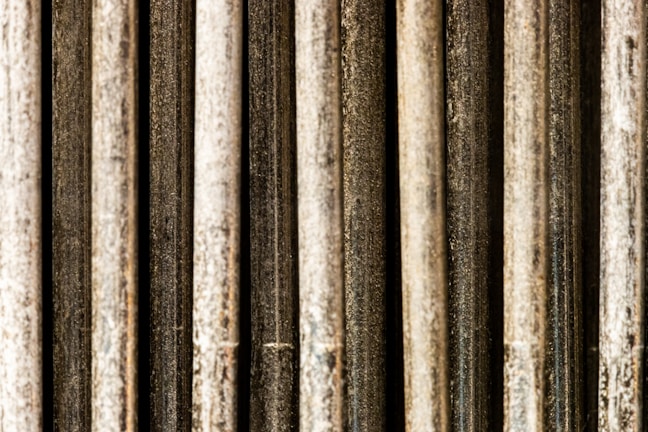 Vertical metal rods with a textured and weathered appearance, aligned in parallel and closely packed together.