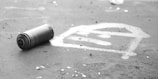 A spray paint can is lying on a surface next to a graffiti symbol that resembles a stylized eye or abstract pattern. The environment appears to be outdoors and rough, with scattered small debris around.