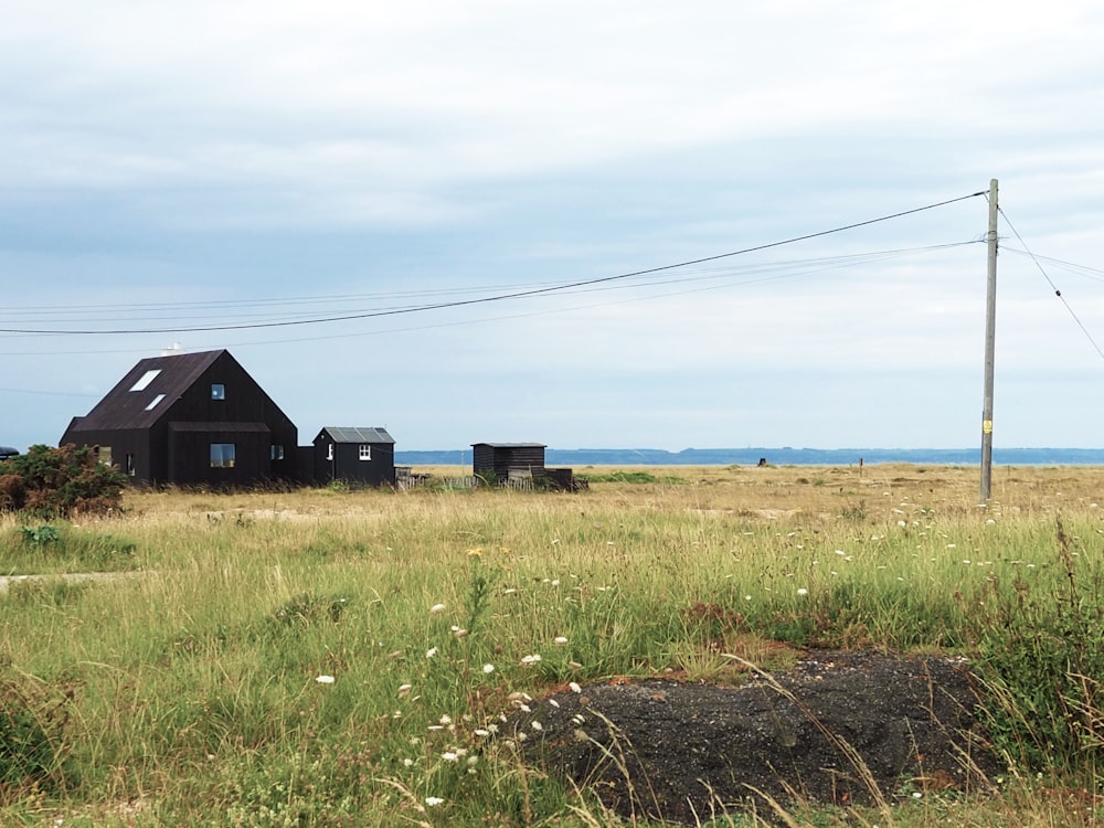 casa de madera negra en campo de hierba verde bajo el cielo azul durante el día
