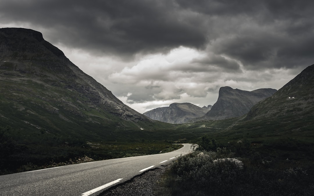 gray asphalt road between green grass field and mountains under white cloudy sky during daytime