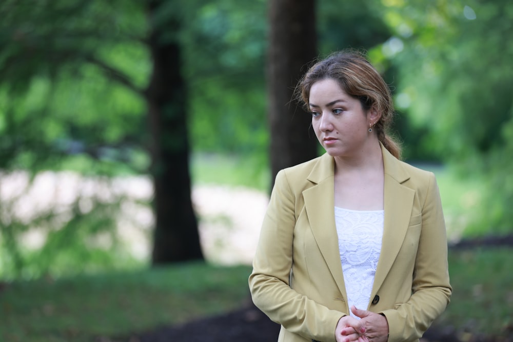 woman in beige blazer standing near green grass during daytime