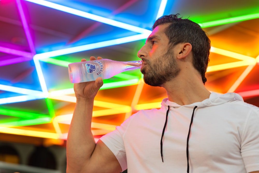 hombre con camiseta blanca de cuello redondo bebiendo de la botella