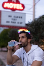 man in white crew neck t-shirt drinking water from blue plastic bottle