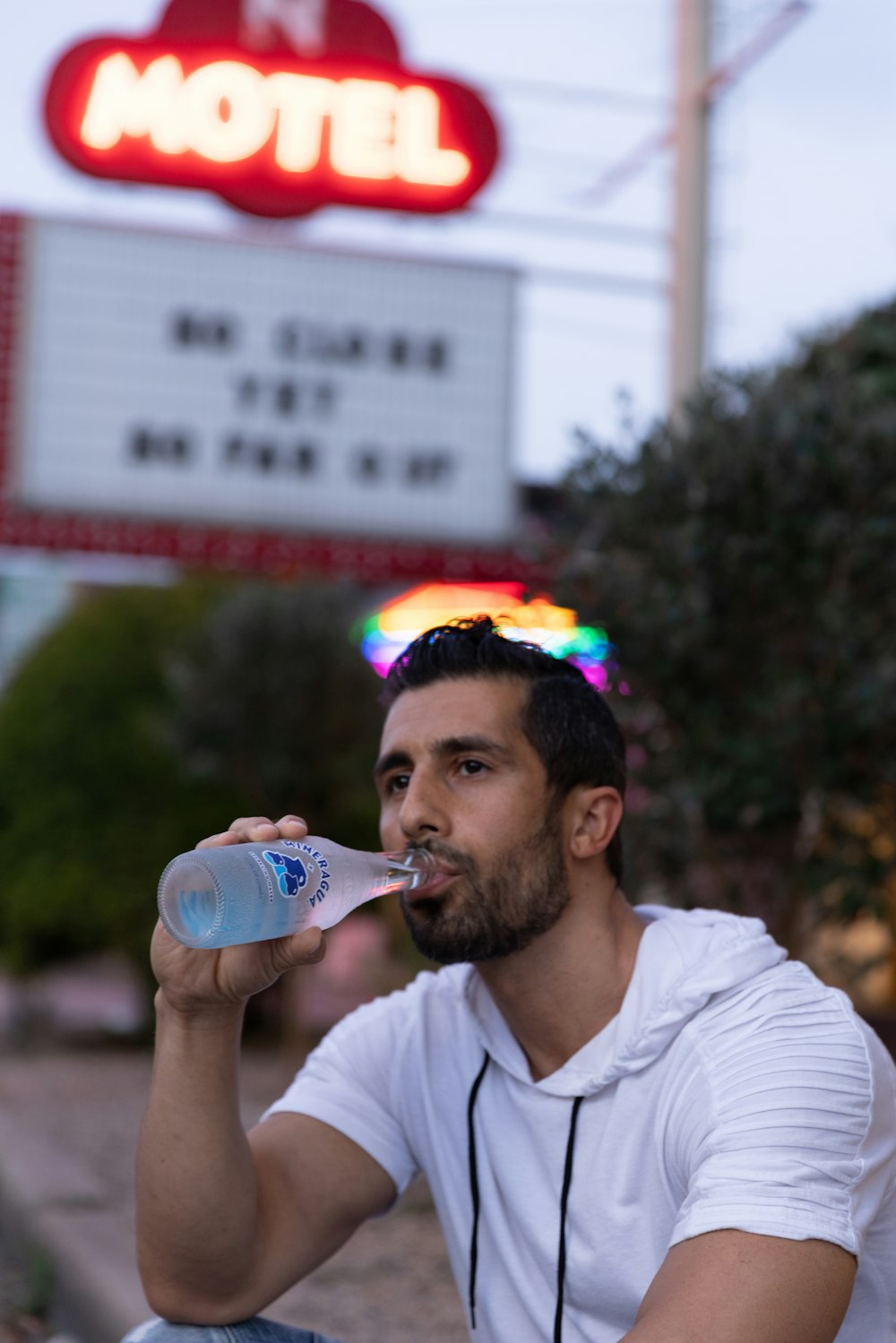 흰색 크루넥 티셔츠를 입은 남자는 파란색 플라스틱 병에서 물을 마신다