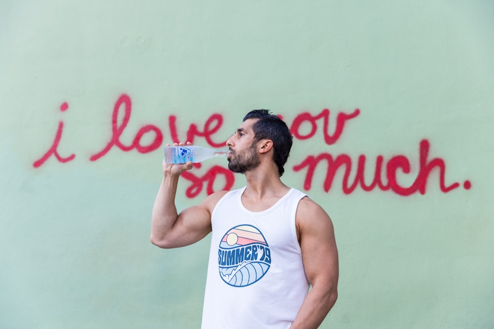 man in white tank top drinking water