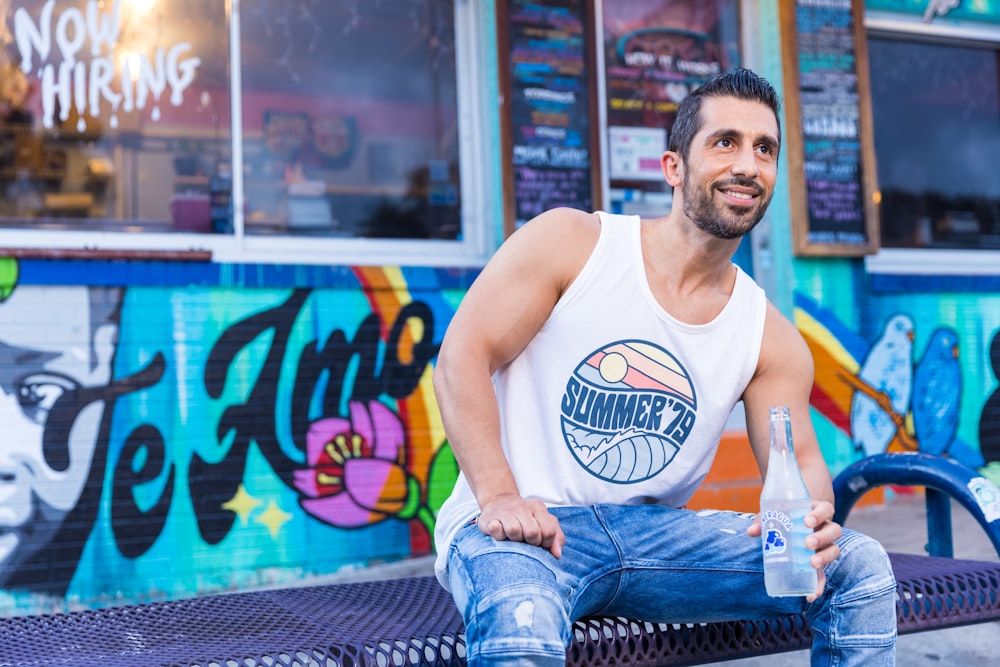 hombre con camiseta blanca sin mangas y jeans de mezclilla azules sentado en una silla azul