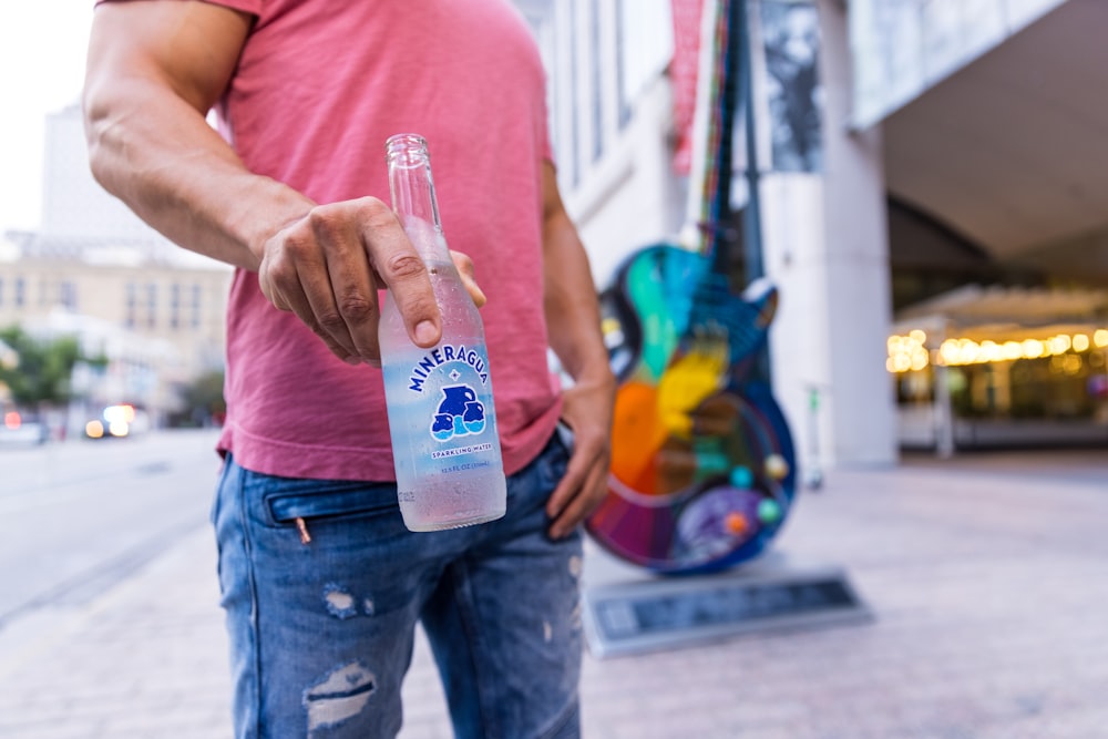 man in pink tank top holding clear plastic bottle