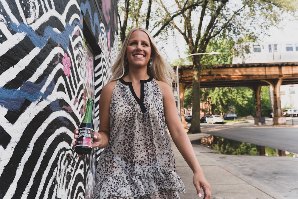 woman in black and white sleeveless dress standing beside white and black wall with graffiti during