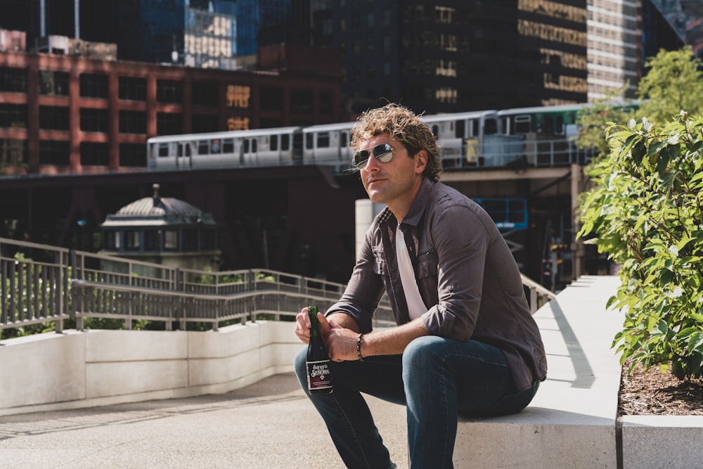 man in gray jacket and blue denim jeans sitting on white bench during daytime