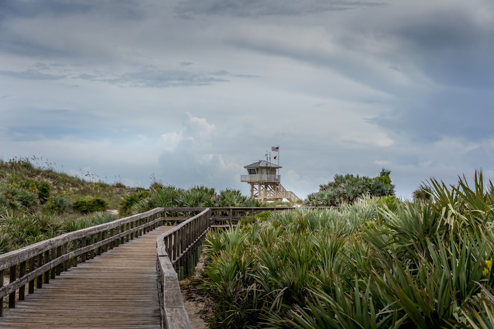 brown wooden dock near white lighthouse under white clouds during daytime