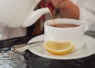 person pouring white ceramic teapot to white ceramic teacup
