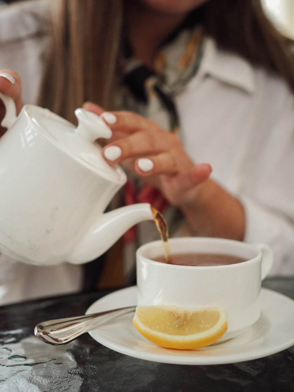 person pouring white ceramic teapot to white ceramic teacup